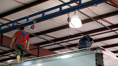 Workers on top of a semi-trailer while using tether track ceiling mounted fall protection.